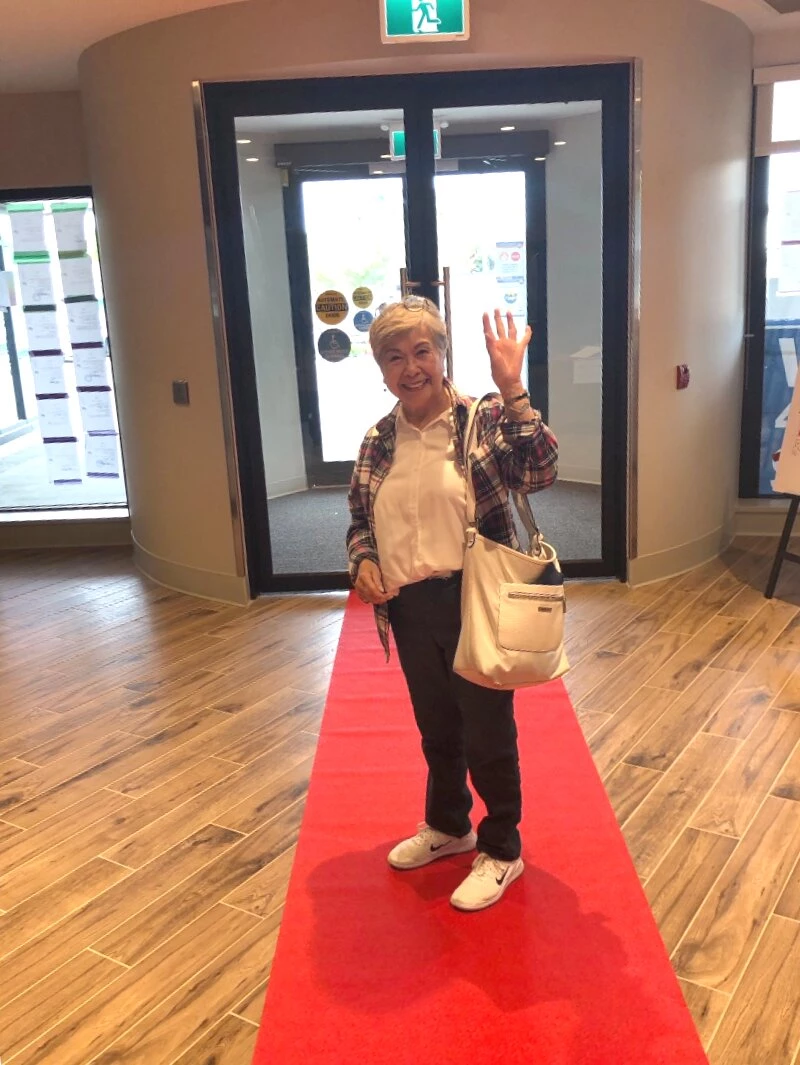 An elderly lady smiling and waving her hand saying hello