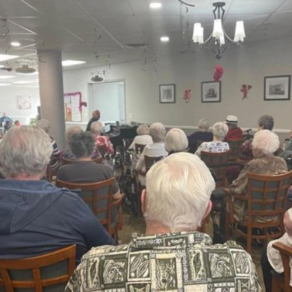 From behind the seniors we see a performance they are watching. The man performing is playing the piano and singing.
